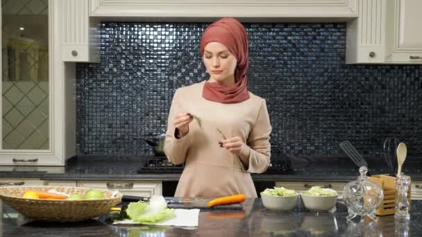 Oriental mujer stands en cocina mesa y come greens — Vídeos de Stock