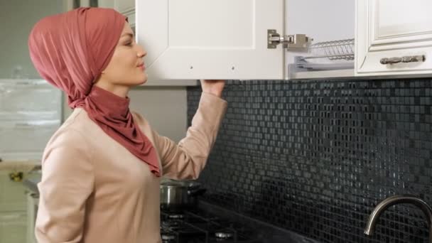 Donna in hijab apre armadio da cucina e prende piatti puliti — Video Stock