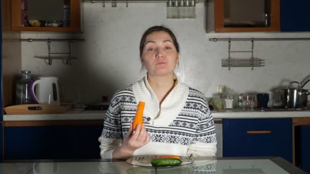 Девушка сидит за обеденным столом и ест морковку — стоковое видео