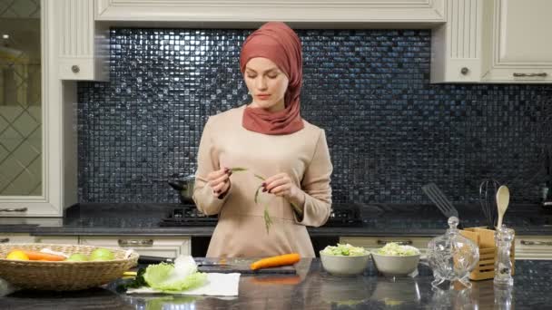 Восточная женщина стоит за кухонным столом и ест зелень — стоковое видео
