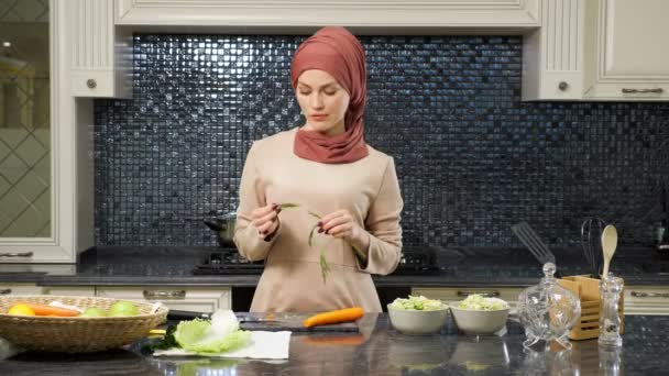 Oosterse vrouw staat aan keukentafel en eet greens — Stockvideo