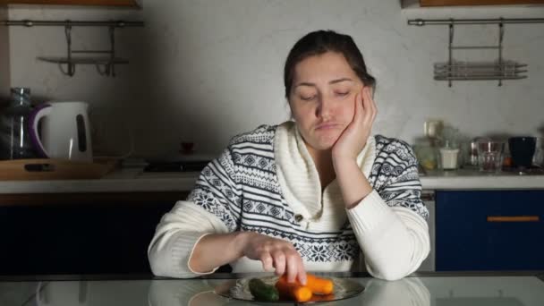 Девушка сидит за обеденным столом и смотрит на тарелку с овощами — стоковое видео