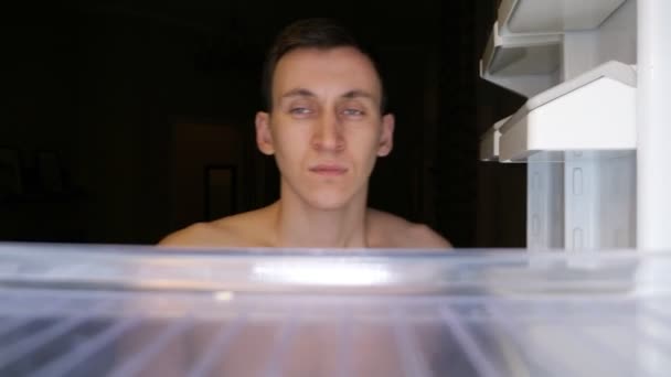 Позіхання хлопець відкриває незаповнений холодильник, щоб знайти їжу крупним планом — стокове відео