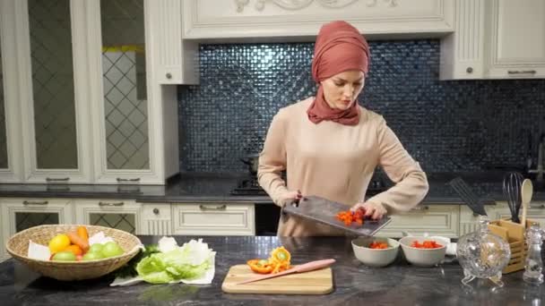 Femme en hijab se tient à la table de cuisine coupe légumes — Video