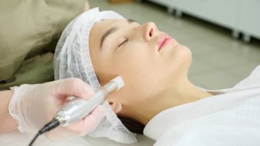 Yeşil ceketli kadın yüzünden mikro dermabrüksiyon uyguluyor.