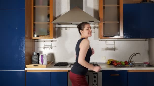 Allegra ragazza balla e canta divertirsi in cucina di casa — Video Stock
