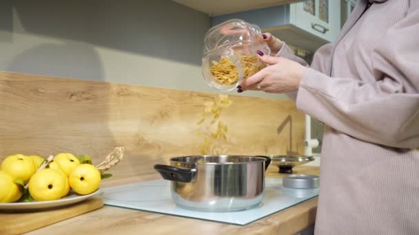 Женщина готовит ужин и наливает пасту в кастрюлю на плите — стоковое видео