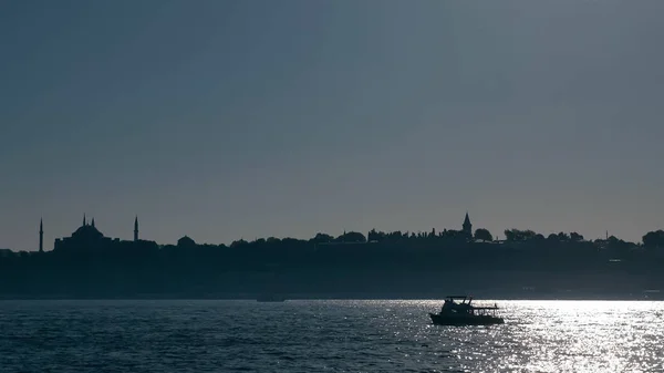 Лодка плавает в сверкающем море против городских силуэтов в сумерках — стоковое фото