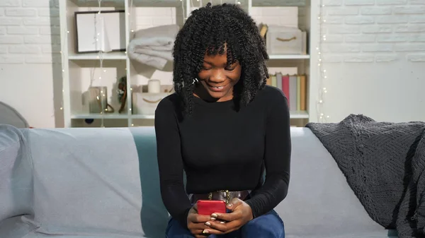 Chica afroamericana mira el teléfono inteligente y se convierte en feliz —  Fotos de Stock