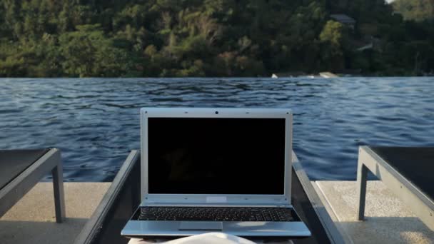 Laptop on person legs with dark screen against hill and pool — 비디오