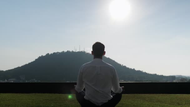 Man meditates on grass on sunny day against big green hill — Stock videók