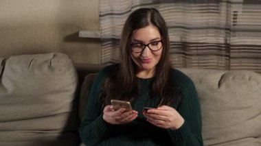 İnternetten alışveriş. Kadın telefon ve kartla oturuyor.