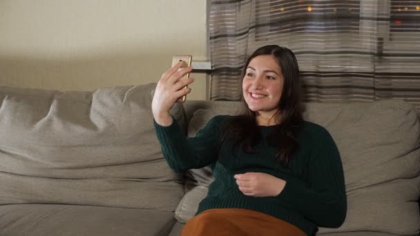 Жінка з Брюнета робить селфі, сидячи на дивані. — стокове відео