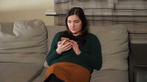 Jeune femme assise sur un canapé avec un téléphone — Video