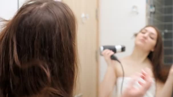 Young woman dries hair with hairdryer reflecting in mirror — Stock Video