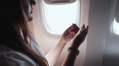 Esmer kadın lombozdan dışarı bakarken ellerine krema sürüyor.