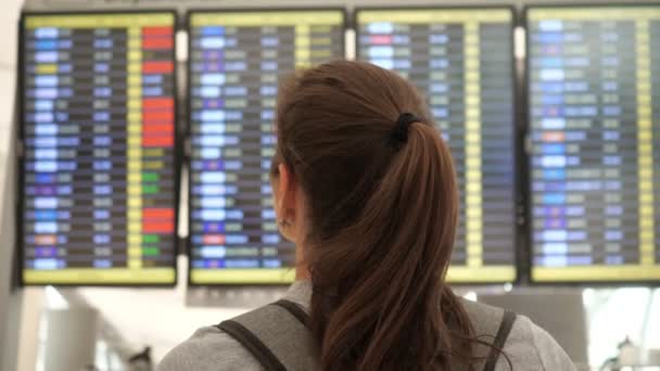 Брюнетка рассматривает расписание вылетов в терминале аэропорта — стоковое видео