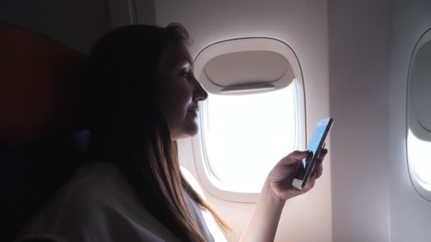 Signora in grigio t-shirt guarda il telefono contro oblò luminoso — Video Stock