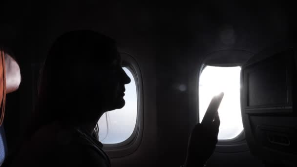 Sziluett lány ül okostelefon ellen ablak repülőgép — Stock videók