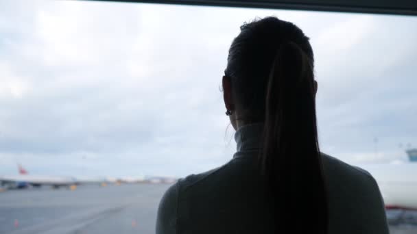 Frau mit Pferdeschwanz betrachtet Flugzeuge auf dem Vorfeld des Flughafens in Nahaufnahme — Stockvideo