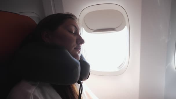 Молодая женщина спит с подушкой на шее против иллюминатора крупный план — стоковое видео
