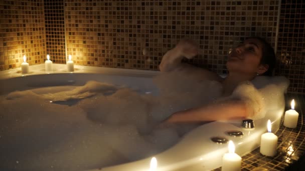 Güzel bir kadın mum ışığında köpük banyosunda yatıyor. — Stok video