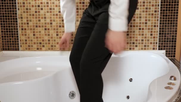 Мужчина в брюках и рубашке лежит в пустой ванне — стоковое видео