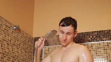 Genç adam duş başlığını tutuyor ve kendini yıkıyor.
