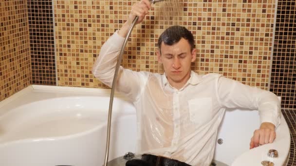 Mann in Hemd und Hose liegt in der Badewanne unter der Dusche — Stockvideo