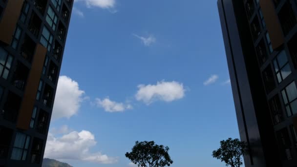 Bulutlar mavi gökyüzünde modern binalar arasında süzülür. — Stok video