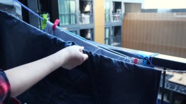 İnsan elleri balkon ipinde ıslak pantolonu mandallarla tamir eder.