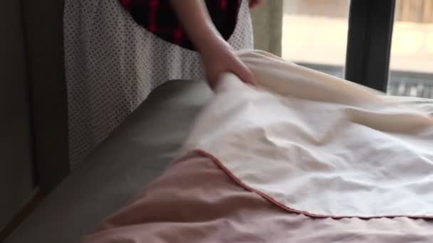 Mulher na camisa cobre cama grande com cobertor marrom no quarto — Vídeo de Stock