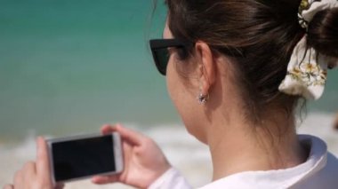 Genç esmer kadın kumsalda video çekiyor.