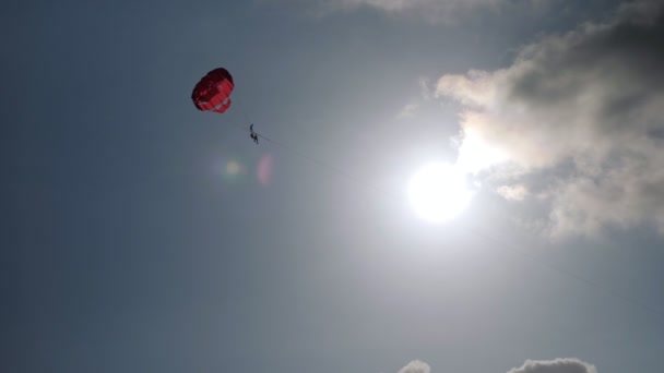 Turist açık mavi gökyüzünde kırmızı paraşütle paraşüt yapıyor. — Stok video