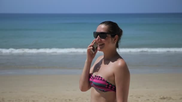 Chica en bikini tiene conversación en el teléfono inteligente en la playa — Vídeo de stock