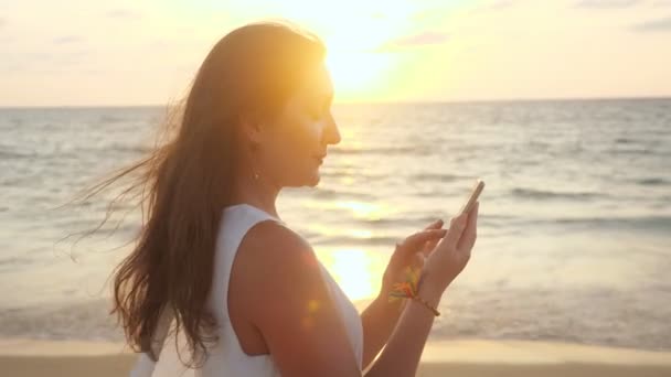 Usmívající se dívka používá smartphone na pláži v tropickém letovisku — Stock video