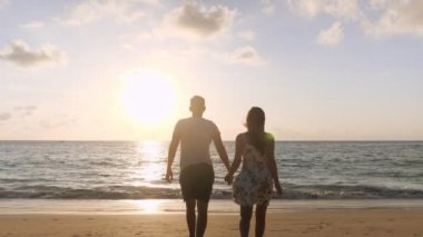 Sahilde okyanus sörfüne yürüyen mutlu çiftin silueti.