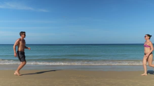 Alegre joven pareja corre y abrazos en la soleada playa cerca del océano — Vídeos de Stock