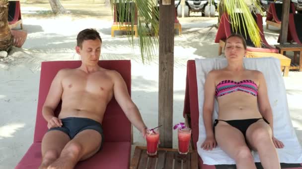 Couple lies on sunbeds and drinks tasty beverages under shed — Stock Video