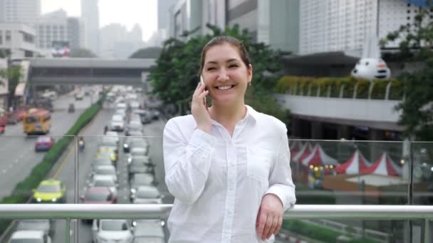 Mujer joven habla en un teléfono inteligente blanco y sonríe alegremente — Vídeo de stock