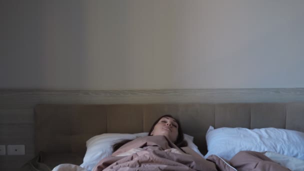 Κυρία ξυπνά σε μεγάλο κρεβάτι με μπεζ κουβέρτα στο δωμάτιο του ξενοδοχείου — Αρχείο Βίντεο