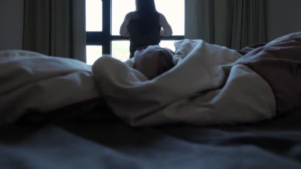 Wanita berambut cokelat membentang melihat keluar jendela di kamar hotel — Stok Video