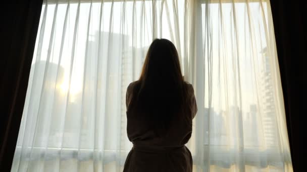 女の子のシルエットがホテルの窓の透明カーテンを開く — ストック動画