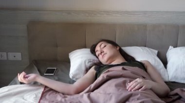 Kadın, oteldeki büyük yatakta uyanan akıllı telefona bakıyor.