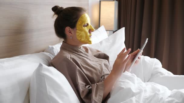 Κυρία με χρυσή μάσκα surfs internet στηρίζεται σε μαλακό κρεβάτι — Αρχείο Βίντεο