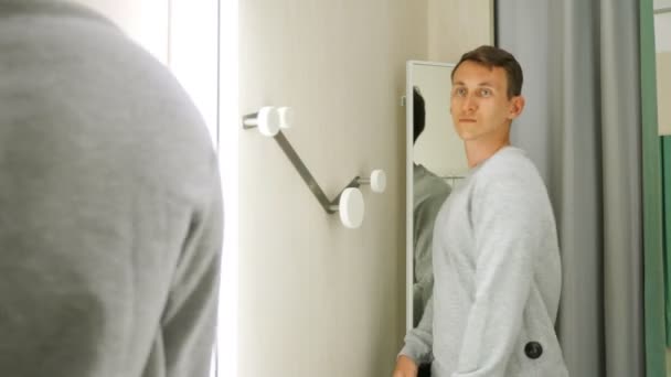 Νεαρός που δοκιμάζει γκρι πουλόβερ μπροστά σε καθρέφτη. — Αρχείο Βίντεο