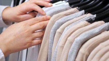 Kadın eli, elbise mağazasındaki askıda duran pamuklu kazakları sınıflandırır..