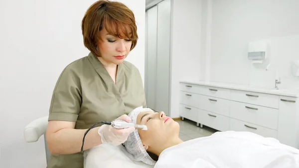 Senhora em casaco verde faz procedimento de microdermoabrasão no rosto — Fotografia de Stock