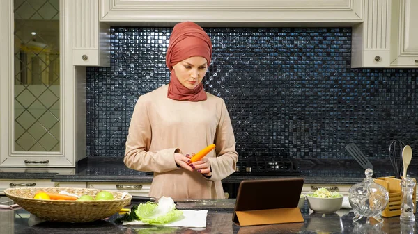 Islam mujer toma zanahoria para cortar viendo halal plato receta — Foto de Stock