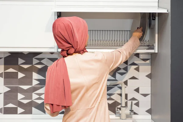 Мусульманка в хиджабе открывает кухонный шкаф на современной кухне — стоковое фото